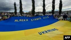 Демонстранты держат гигантский украинский флаг на митинге в поддержку Украины вдоль шоссе Сьюард в Анкоридже, штат Аляска, 14 августа 2025 года, накануне запланированной встречи президентов США и России