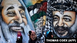 Палестински жени минават покрай стенопис, изобразяващ покойния духовен лидер на Хамас шейх Ахмед Ясин и покойния палестински лидер Ясер Арафат на 4 май 2014 г. в град Газа.