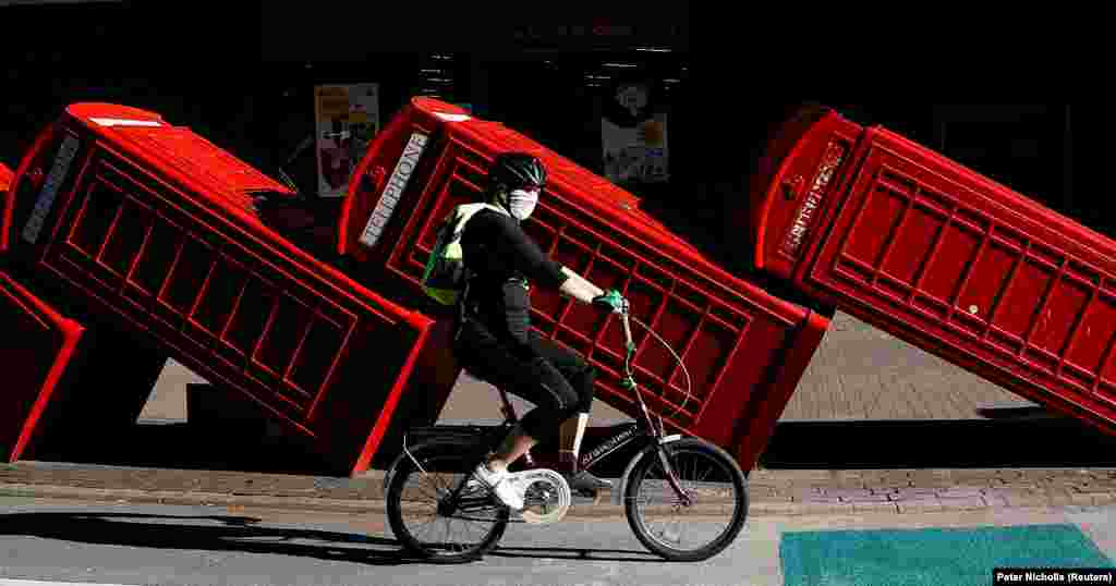 Велосипедист едет в защитной маске мимо инсталляции &laquo;Out of Order&raquo; скульптора Дэвида Мача. 12 красных телефонных будок классической модели, которые являются столь же узнаваемым символом Великобритании, как и почтовые ящики и двухэтажные автобусы, сложены в стороне по принципу &laquo;домино&raquo;