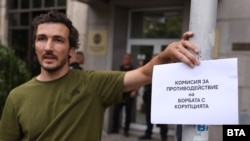 Снимката е илюстративна. На нея протестиращ държи плакат с надпис "Комисия за противодействие на борбата с корупцията" пред сградата на Комисията за противодействие на корупцията в София, 9 юли 2025 г.