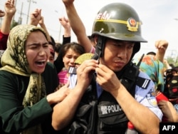 Egy ujgur asszony fog meg egy kínai rohamrendőrt egy tüntetésen Urumcsi városában Xinjiang tartományban 2009. július 7-én