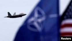 Zastave NATO-a i SAD-a se vijore dok u pozadini prolazi američki borbeni avion (fotoarhiv)