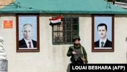 Руски военен стои на пост между портретите на сирийския президент Башар ал-Асад (вдясно) и руския президент Владимир Путин (вляво), висящи пред пост за охрана на контролно-пропускателния пункт Wafideen в покрайнините на Дамаск, 1 март 2018 г.