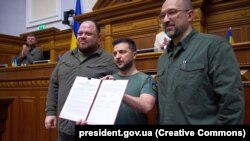 Volodimir Zelenski (centru), alături de prim-ministrul Denis Șmihal (dreapta) și președintele Radei, Ruslan Ștefanciuk, prezintă parlamentarilor declarația comună privind obținerea statutului de membru UE, 1 iulie