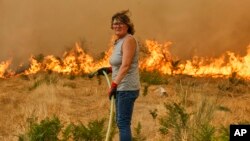 O femeie încearcă să stingă focul, cu un furtun, în timpul unui incendiu forestier în Santa Baia De Montes, nord-vestul Spaniei, 14 august 2025.