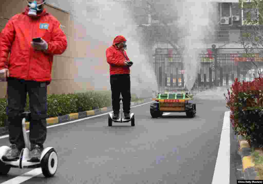 Работници со заштитни маски на самобалансирачки скутери контролираат роботски испрскувач на средство за дезинфекција меѓу станбени згради во Вухан, епицентарот новиот коронавирус, во Кина на 3 март. 