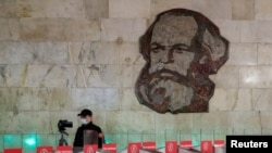 Radnik obezbeđenja sa zaštitnom maskom, ispod mozaika Karla Marksa, na ulazu u moskovski metro 1. maja 2020.