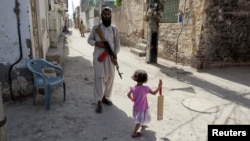A girl with a cricket bat walks past a militant in Rahim Yar Khan, southern Punjab Province (file photo)