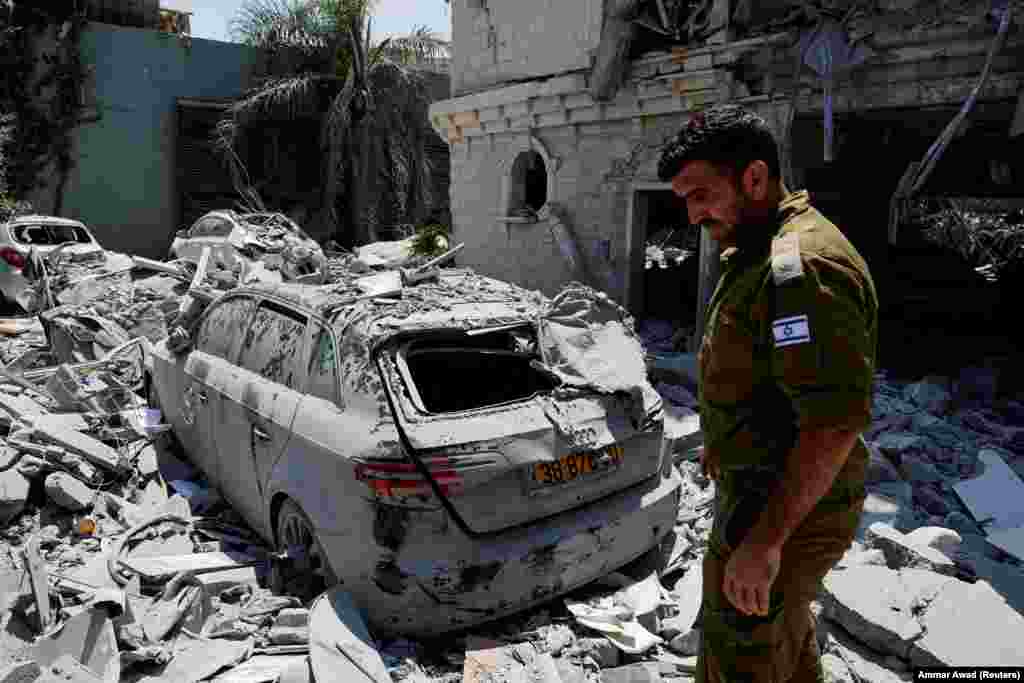 Një ushtar izraelit duke qëndruar pranë një automjeti të dëmtuar pasi raketat e lëshuara nga Irani goditën një ndërtesë banimi në Tamra, veri të Izraelit, më 15 qershor.