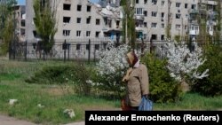 Žena tokom proslave pravoslavnog Uskrsa, dok se u pozadini vidi stambena zgrada oštećena tokom rusko-ukrajinskog sukoba, u Avdijevki, u oblasti Donjeck, oblast Ukrajine pod ruskom kontrolom, 20. aprila 2025. 