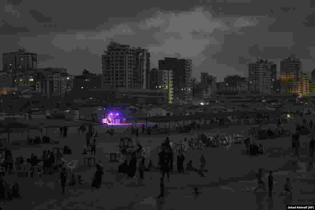 Një tezgë e ndriçuar veçohet teksa palestinezët freskohen në Detin Mesdhe, pas perëndimit të diellit, afër portit të Qytetit të Gazës.