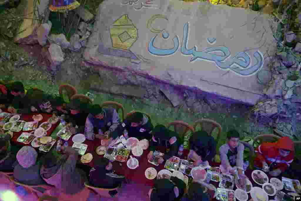 Mbishkrimi &quot;Ramazan&quot;, i shkruar arabisht. Palestinezët duke ngrënë syfyrin e parë të shtruar në mënyrë kolektive pranë shtëpive të tyre të shkatërruara në Han Jounis, në jug të Rripit të Gazës, të premten, 28 shkurt 2025.&nbsp;