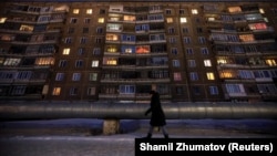 Женщина идет на фоне панельного жилого дома советской постройки. 