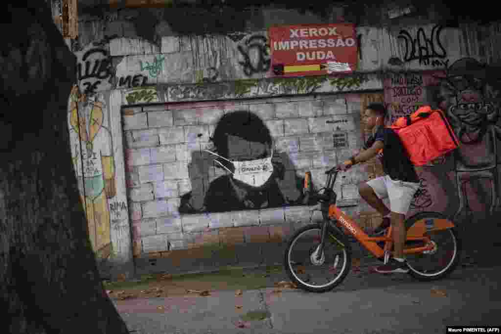 Маж вози покрај графит на бразилскиот претседател Жаир Болсонаро, со маска за лице на ѕид во центарот на Рио де Жанеиро. Болсонаро ги отфрли ризиците што ги носи коронавирусот.