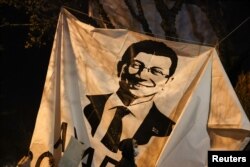Një person duke ecur afër banerit me fotografinë e kryetarit të Stambollit, Ekrem Imamoglu në një protestë kundër ndalimit të tij.