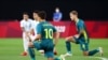 Az argentin és az ausztrál válogatott tagjai fél térdre ereszkednek a 2021-es tokiói olimpia egyik első labdarúgó-mérkőzésén