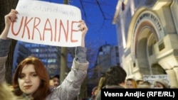 Učesnica protesta nosi transparent sa porukom "Stojimo sa Ukrajinom" 