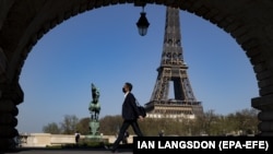 Pješak sa maskom uživa u toplom proljetnom vremenu hodajući mostom Bir Hakeim u blizini Eiffelovog tornja u Parizu, Francuska, 31. marta 2021.