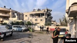 Banorë dhe zyrtarë policorë shihen afër shtëpisë së goditur në qytezën Tira të Izraelit, me predha të Libanit. 