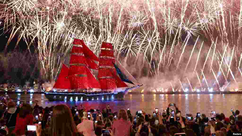 Gledaoci posmatraju vatromet na nebu i brod sa crvenim jedrima koji plovi duž reke Neve tokom svečanosti u čast maturanata u Sankt Peterburgu.