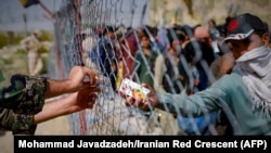 Një ushtar iranian duke u dhënë lëngje refugjatëve afganë të mbledhur në kufirin mes Iranit dhe Afganistanit. Gusht 2021.