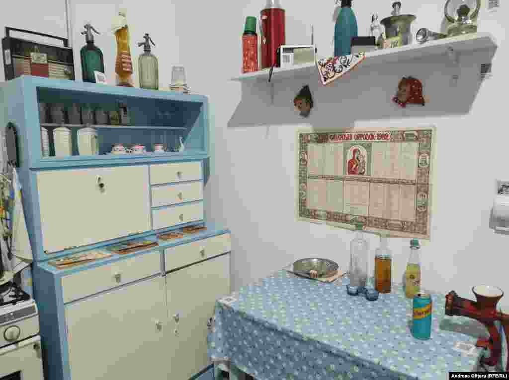 Muzeul Comunismului din București. Bucătăriile din acea vreme arătau toate aproape la fel. Dulapul din imagine a fost recondiționat, dar arată la fel ca pe vremea când era folosit. Pe dulap, un radio VEF, fabricat în Letonia (parte, la acel moment, a URSS), la care se putea asculta, pe unde scurte, însă puternic bruiat, Radio Europa Liberă. Sifoanele (tot de pe dulap) erau nelipsite în orice casă. Apa minerală nu se găsea, așa că sifonul umplut &bdquo;la sifonăria din colț&rdquo; era soluția pentru apă carbogazoasă. În toate bucătăriile exista și celebra mașină de tocat carne, al cărei cuțit trebuia ascuțit, din când în când, la tocilărie. Lampa cu gaz din dreapta sus era folosită aproape în fiecare zi, când se &bdquo;lua lumina&rdquo;.