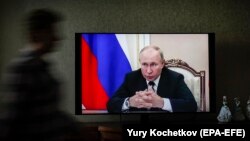 Një grua kalon pranë një ekrani ku shihet president rus, Vladimir Putin.
