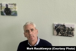 Pol Niland stoji na stubištu Lajflajn Ukrajine, gdje vise slike ratnih veterana iz Donbasa, od kojih mnogi rade kao operateri u pozivnom centru za prevenciju samoubistava.