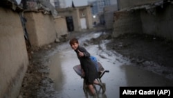 FILE: An Afghan boy gives a thumbs-up as he pushes a wheelbarrow through a muddy lane at a displacement camp in Kabul in November 2019.
