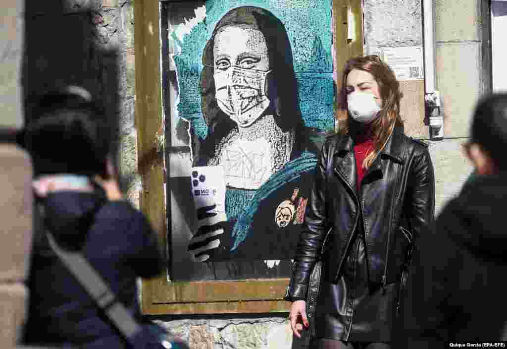 Туристка во Барселона, Шпанија, позира покрај графити на кои се гледа како Мона Лиза носи маска.