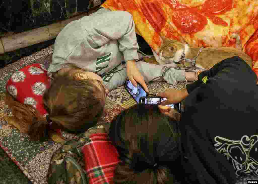 Dy banore të Kievit, të shtira në dyshemenë e metrosë, duke shikuar telefonat mobilë, më 12 korrik.