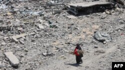 O femeie palestiniană cară crengi de lemn, în timp ce trece pe lângă dărâmăturile și ruinele din cartierul al-Tuffah al orașului Gaza, pe 14 august 2025.