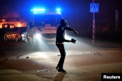Një person duke hedhur gur në drejtim të veturës së policisë gjatë trazirave të dhunshme në Malmo, Suedi, 3 shtator 2023.