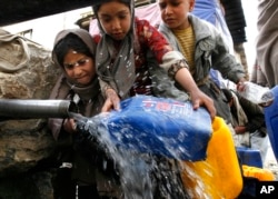 Egy lány vizet vesz a nyilvános csapból, miközben mások megpróbálják elvágni a csövet. (archív fotó)