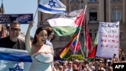 Reprezentanta Israelului Yuval Raphael pășește pe covorul turcoaz la ceremonia de deschidere a Eurovision 2025, pe fundalul protestatarilor care țin drapele palesteniene și pancarte prin care cer eliminarea Israelului din concurs. Basel, Elveția, 11 mai 2025.