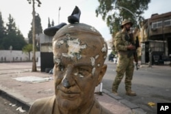 Боец от опозицията до счупен бюст на покойния сирийски президент Хафез Асад с чифт обувки върху главата му, Дамаск, Сирия, 11 декември 2024 г.