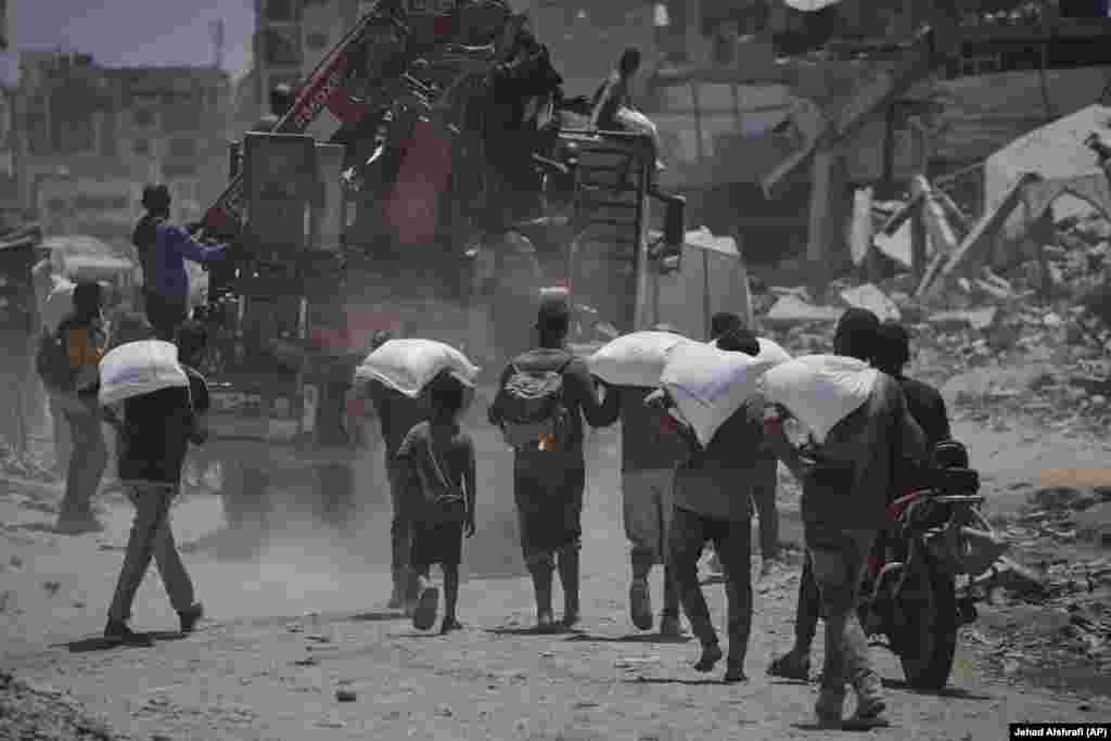 Palestinezë duke bartur thasë me miell, që i morën nga organizatat humanitare, më 22 korrik.