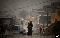 Egy nő műanyag kannában cipel vizet haza, miközben felfelé kapaszkodik egy emelkedőn Kabulban. (archív fotó)