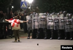 Протестувальник, загорнутий у прапор Грузії, йде у напрямку поліцейських під час опозиційного мітингу в день місцевих виборів у Тбілісі, Грузія, 4 жовтня 2025 року