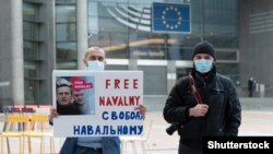 Két ember Brüsszelben egy Navalnij szabadon engedését követelő táblát tart. 2021. január 19.