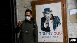 Čovjek sa zaštitnom maskom pored postera umjetnika TVBoy sa ujakom Samom na kojem piše “Hoću da ti ostaneš kući”, Barselona, Španija, 14. mart, 2020. 