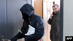 Președintele Asociației jurnaliștilor din Belarus, Andrei Bastunets (dreapta) și un polițist părăsesc sediul Asociației după un raid din februarie 2021.