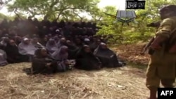 Кадр с видеозаписи, на которой похищенные в Нигерии школьницы, одетые в хиджабы, поют суры из Корана под присмотром вооруженного человека