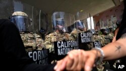 Protestuesit shtrëngojnë duart para një rreshti të Gardës Kombëtare të Kalifornisë në një Ndërtesë Federale në qendër të Los Anxhelosit, 9 qershor 2025.