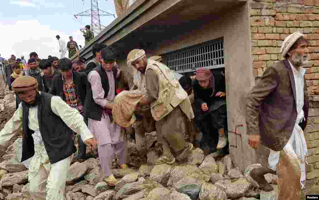 Men carry an injured person out of a house on August 26 after floods hit Charikar, the capital of Parwan Province.