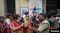 Policijski službenik traži od žena koje su došle primiti dozu vakcine protiv COVID-19 da čekaju u redu, ispred centra za vakcinaciju u Ahmedabadu u Indiji, 30. srpnja 2021. 