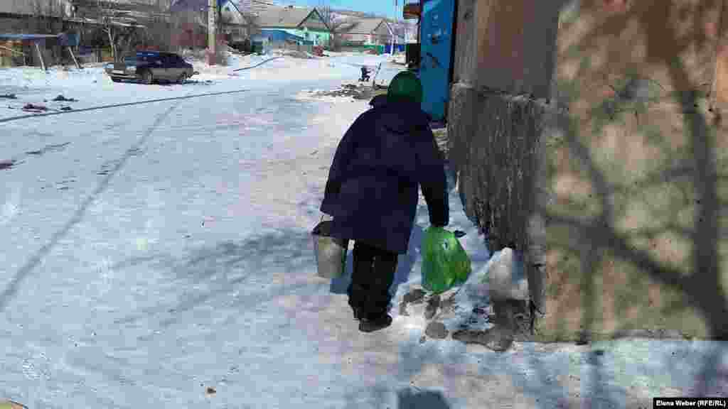 Пенсионерка несет ведро с углем в свою квартиру.