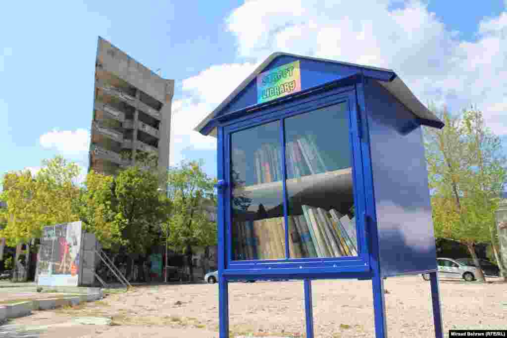 Jedna od uličnih biblioteka u Mostaru postavljena je i u centru grada, na bivšoj, ratnoj liniji razdvajanja. U pozadini se vidi porušena zgrada, među Mostarcima do 1992. godine poznata i kao “Staklena banka” 