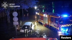 Rescuers push a partially submerged car on a flooded street following unprecedented rainfall in Odesa in this handout picture released on October 1, 2025.